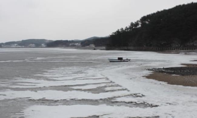 A small boat on a frozen sea next to the shoreline
